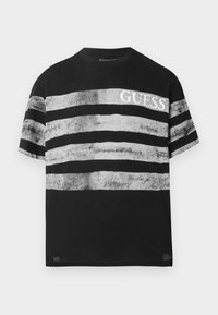 Čierne tričko s krátkym rukávom a sivými horizontálnymi pruhmi. Na hrudi sa nachádza logo "GUESS" v bielej farbe. Bavlnený materiál s jemnou textúrou.
