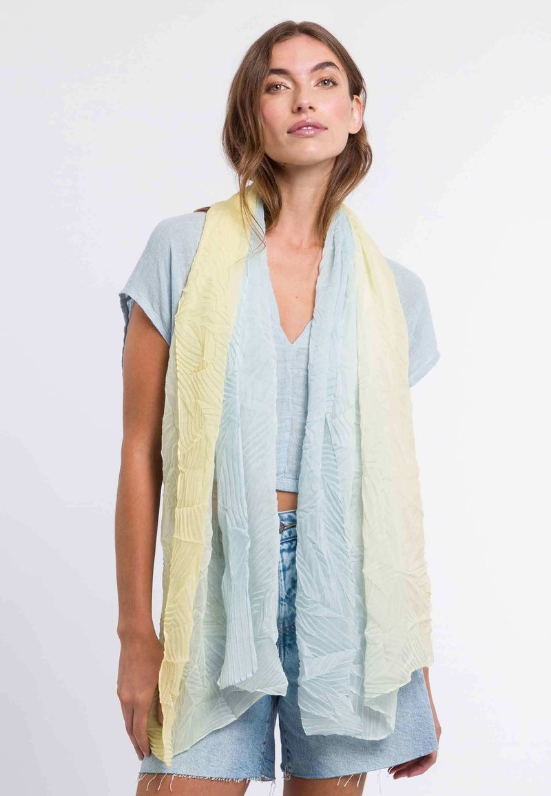 Scarf leggero e textured in un gradiente di giallo pastello a blu, caratterizzato da intricate pieghe. Indossato in modo sciolto sopra un outfit casual.