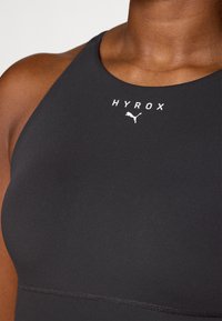 Top atlético preto com gola alta, costuras planas e logótipo branco "HYROX" com ícone de gato ao centro. Adequado para desporto e exercício.