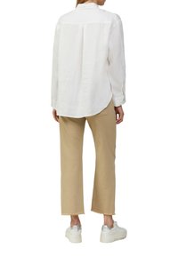 Witte linnen blouse met lange mouwen en een achterpand, gecombineerd met beige cropped broeken en witte sneakers met zilveren zool.