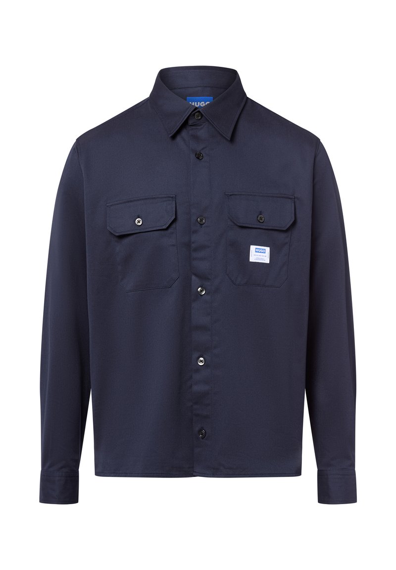 Camisa de botones azul marino de manga larga, con dos bolsillos en el pecho y un pequeño parche de logo. Hecha de tela suave con un cuello clásico.