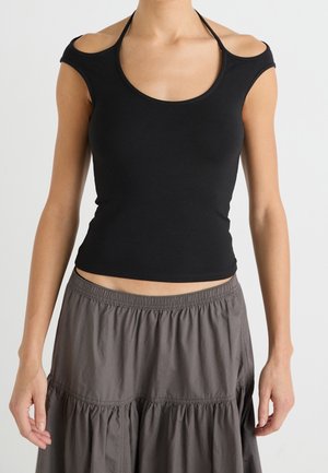 Femme portant un haut noir à épaules dénudées avec des bretelles halter et une jupe ample gris foncé taille haute.