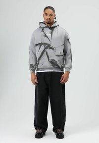 Grijze tie-dye hoodie met een voorzak en een wit tekstlogo; gecombineerd met zwarte baggy jeans en zwarte schoenen met roze veters.