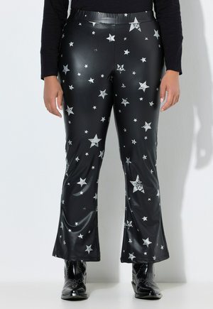 Sorte bukser i imiteret læder med sølvstjerner, let udvidede ben, båret med sorte ankelstøvler med nitter og en sort top med lange ærmer.