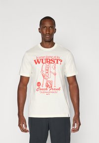Cream cotton t-shirt featuring a red graphic print of a cartoon hot dog golfer with text saying "Is your game at its WURST?" and "Call Coach Frank."