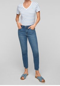 Vit och blå randig t-shirt med V-ringning, matchad med blå smala jeans. Fötter i blå knutna flatsandaler med ljusa sulor.