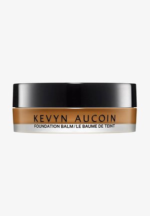 Baume de la Fondation Kevyn Aucoin dans un contenant rond, noir et transparent. Le produit est de couleur tan chaud avec une texture lisse.