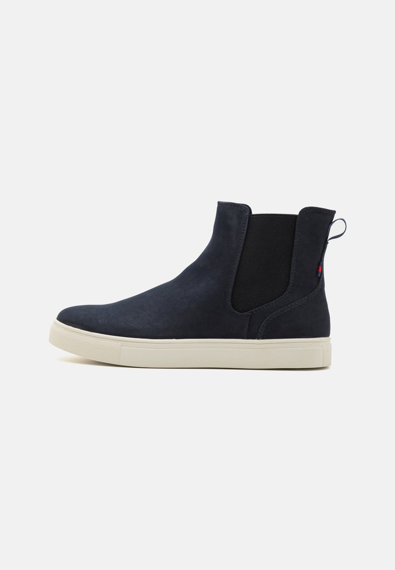 Marineblå ankelstøvletter i suede med elastiske sidepaneler og en struktureret beige gummisål. Har en strop og et minimalistisk design.