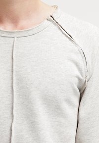 Sudadera de color gris claro hecha de una tela suave, con un escote de borde sin rematar y mangas raglán con detalles de costura visibles.
