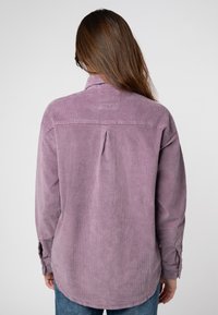 Paarse corduroy shirt met een relaxte pasvorm, voorzien van een subtiele rugplooien en knoopmanchetten. Zachte textuur met verticale ribben en een afgeronde zoom.