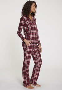 Pajama set s červenobílým kostkovaným vzorem, obsahující dlouhý rukáv s límečkem a kapsou, doplněný rovně střiženými kalhotami. Měkký, bavlněný materiál.