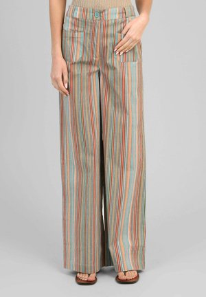 Femme portant un pantalon à jambes larges avec des rayures verticales en bleu, orange, rouge et beige, associé à un haut beige et des sandales.