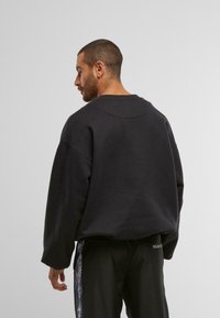 Felpa nera over size con scollatura tonda e spalle cadenti, realizzata in un tessuto morbido. Accentuata da una texture liscia e un design minimale.