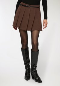 Gonna plissettata marrone con una cintura nera, abbinata a stivali neri in pelle al ginocchio e collant neri trasparenti. Design semplice, texture liscia.