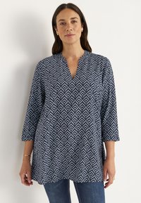 Navy blue tunic with a geometric white pattern, v-neckline, and three-quarter sleeves, made of lightweight fabric.