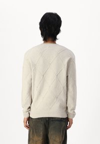 Light beige knitted sweater with a diamond pattern, ribbed cuffs, and hem. Features a crew neck and long sleeves. Textured fabric finish.