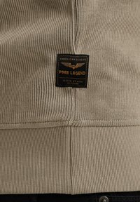 Suéter de color beige con relieve que presenta una etiqueta negra con bordado dorado que dice "PME LEGEND" y "AMERICAN CLASSIC" en el frente.