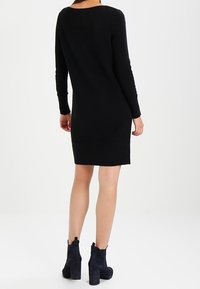 Svart stickad klänning med långa ärmar och en ribbad struktur, med rund halsringning och rak silhuett. Matchad med svarta klackiga ankelstövlar.