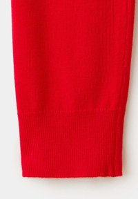Gros plan d'une manche de pull rouge en tricot avec un bord-côte sur fond blanc.