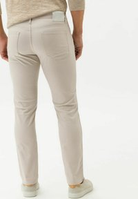 Light beige slim-fit pants with back pockets, a smooth texture, and a neutral design, paired with light-colored sneakers.
