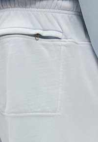 Ανοιχτό γκρι φόρμα με ελαστική μέση και φερμουαρ πίσω τσέπη που φαίνεται στη δεξιά πλευρά.