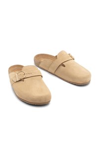 Beżowe zamszowe klapki z zaokrąglonym noskiem, regulowanym paskiem i złotym detalem z klamrą. Korkowa wkładka i gumowa podeszwa zapewniająca przyczepność.