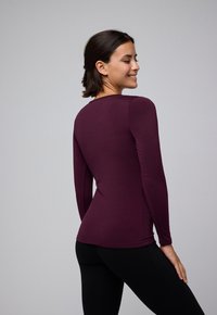 Camiseta de manga larga en púrpura oscuro, con un tejido suave y un diseño entallado, cuello redondo y detalles cosidos a los lados.