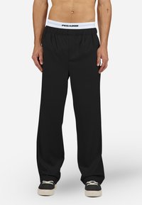 Fekete bő szárú nadrág elasztikus, fehér derékpánttal, amelyen a "PEGADOR" logó látható. Simább anyag, casual kialakítás, látható minták nélkül.