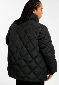 Schwarze, gesteppte Pufferjacke mit hohem Kragen, lockerer Passform und Rautenmuster auf der Oberfläche. Weicher, gepolsterter Stoff für Wärmeisolierung.