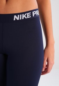 Leggings stretch blu navy con logo Nike Pro su una ampia cintura elastica. Il tessuto è morbido e aderente, progettato per l'abbigliamento sportivo.