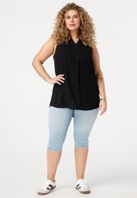 Zwarte mouwloze top met V-hals, gecombineerd met lichtblauwe cropped jeans. Het model draagt witte sneakers met zwarte en bruine accenten.