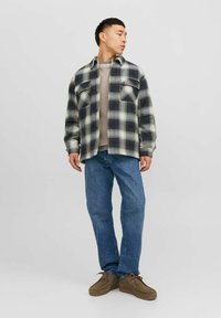 Cămașă flanel cu carouri alb-negru, suprapusă peste un pulover bej, asortată cu blugi și pantofi maro cu șiret. Look casual pentru exterior.