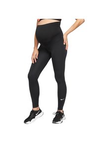 Zwangere vrouw in zwarte zwangerschapsleggings en zwarte Nike sneakers, staand met één hand op de heup en de andere op de dij.
