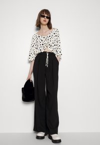 Top curto branco com bolinhas pretas, frente ajustada, calças largas pretas, bolsa de pelo sintético preta e sapatos de plataforma brancos e grossos.