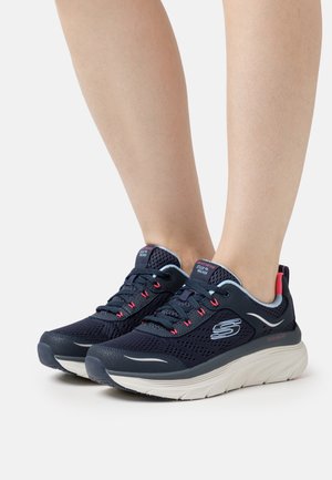 Tmavě modré sportovní boty se síťovaným svrškem, texturovanými detaily, růžovými akcenty, lehkou bílou podrážkou a reflexním logem.