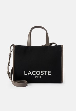 Czarna torba typu tote Lacoste z szarymi uchwytami i paskiem na ramię, tkanina o fakturze oraz biały napis "LACOSTE 1933" z przodu.