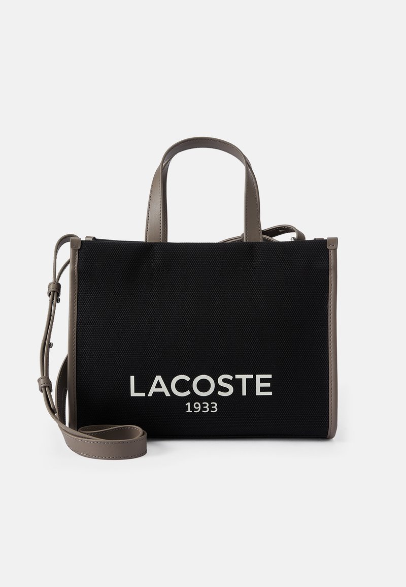 Sac cabas noir Lacoste avec poignées gris et bandoulière, tissu texturé et inscription blanche "LACOSTE 1933" sur le devant.