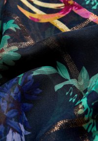 Tissu sombre avec des motifs floraux bleu sarcelle et bleu, des fils métalliques dorés, et des plis créant texture et profondeur.