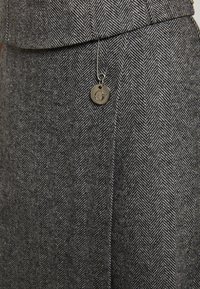 Suknja od vune s dodatkom, u uzorku riblje kosti, sivo- crnih tonova. Uključuje srebrni privjesak pričvršćen sigurnosnom iglom.