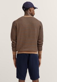 Gestreifter Pullover in Braun und Marineblau, aus Strickstoff gefertigt, mit Rundhalsausschnitt und gerippten Bündchen, kombiniert mit marineblauen Shorts.