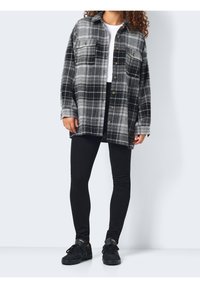 Czarna i biała koszula flanelowa w kratę, zapinana na guziki, z dwoma kieszeniami na piersi, połączona z czarnymi legginsami i czarnymi butami sportowymi. Gładka tekstura.