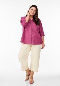 Camicia in lino rosa con scollo a V e maniche arrotolate, abbinata a pantaloni beige a gamba larga e sandali marroni con cinturini.