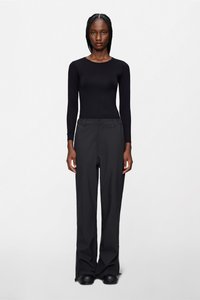 Μαύρο μακρυμάνικο τοπ σε συνδυασμό με μαύρο παντελόνι. Το παντελόνι έχει ίσια γραμμή και ομαλή υφή. Τα παπούτσια είναι μαύρα με στρογγυλεμένη μύτη.