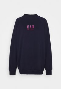 Laivastonsininen collegepaita, jossa korkea kaulus, pitkät hihat ja rento istuvuus. Edessä on vaaleanpunainen kirjailtu "GAP"-logo.