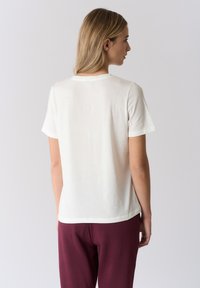 Maglietta bianca in cotone con scollo rotondo e maniche corte, caratterizzata da un taglio dritto e una texture liscia, mostrata di spalle.