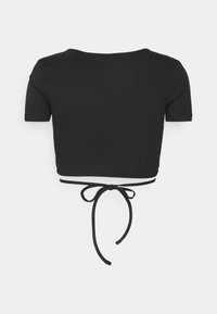 Crop top noir côtelé à manches courtes avec un dos dégagé en forme de coupe et une fine lanière nouée à la taille, présenté sur un fond blanc.