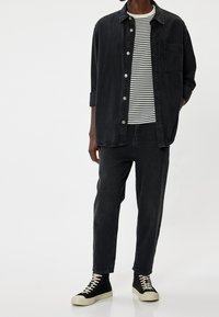 Camisa negra de botones sobre una camiseta de rayas blanco y negro. Jeans oscuros y zapatillas altas negras con suela blanca. Diseño minimalista.