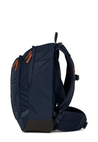 Un sac à dos bleu marine avec des accents en cuir brun, doté de bretelles réglables, de plusieurs poches zippées et d'une forme structurée.