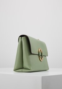 Borsa a tracolla verde in pelle con forma strutturata, hardware circolare dorato e pattina pieghevole. Texture liscia con dettagli di cucitura ordinati.