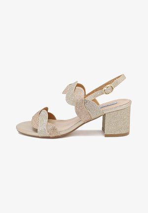 Sandal con tacco a blocco beige e oro con cinturini texturizzati, caratterizzata da un design decorativo a spirale e una chiusura con fibbia sul cinturino alla caviglia.